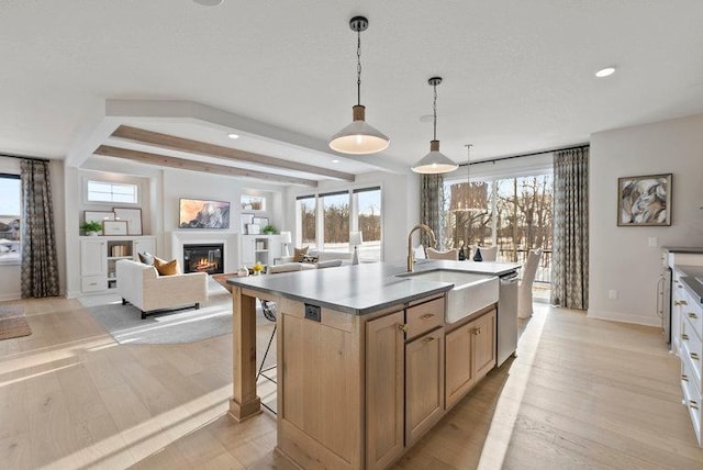 kitchen with a center island with sink, light hardwood / wood-style floors, stainless steel dishwasher, hanging light fixtures, and sink