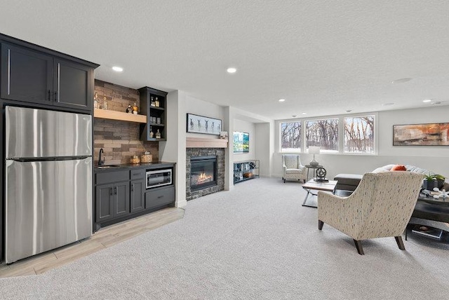 living room featuring light carpet, a textured ceiling, sink, and a stone fireplace