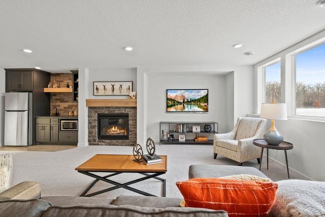 carpeted living room with a textured ceiling, sink, and a stone fireplace