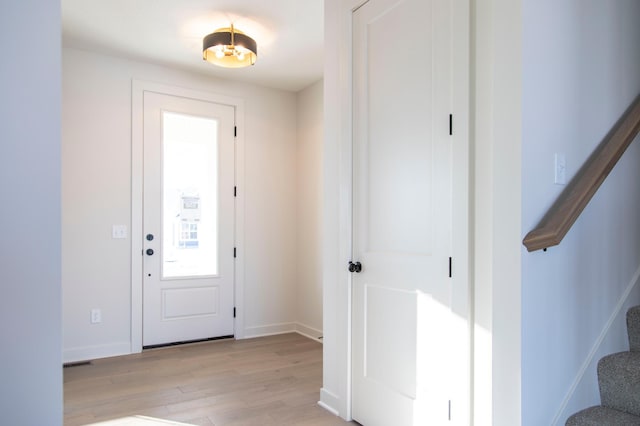 foyer entrance with light wood finished floors, stairway, visible vents, and baseboards