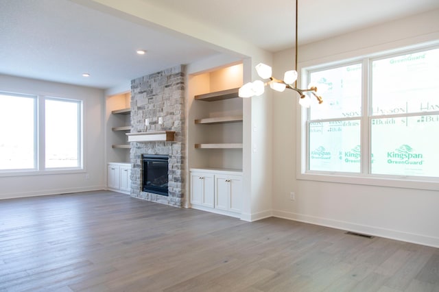 unfurnished living room with visible vents, a stone fireplace, baseboards, and wood finished floors