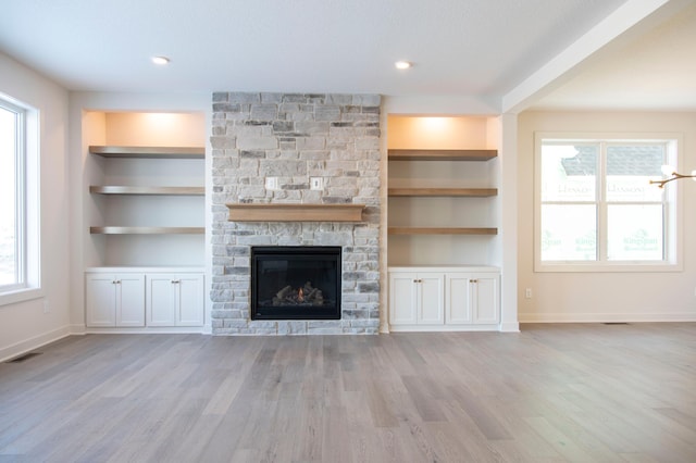 unfurnished living room with built in features, light wood-type flooring, visible vents, and plenty of natural light