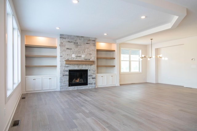 unfurnished living room with visible vents, built in features, light wood-style flooring, a fireplace, and a chandelier