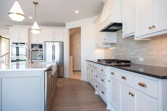 kitchen with dark countertops, appliances with stainless steel finishes, decorative light fixtures, custom exhaust hood, and white cabinetry