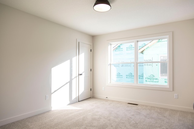 empty room with baseboards, visible vents, and light colored carpet