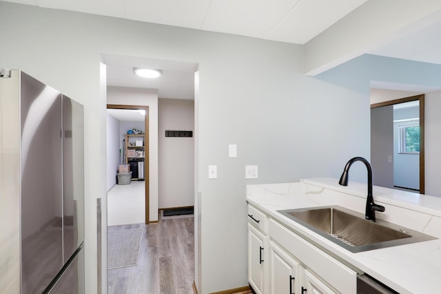 kitchen featuring light wood-type flooring, sink, white cabinetry, stainless steel appliances, and light stone countertops