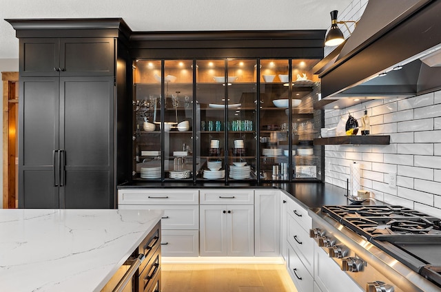 interior space featuring light hardwood / wood-style floors, stainless steel gas cooktop, white cabinets, custom exhaust hood, and dark stone counters