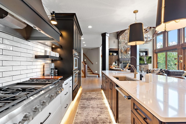 kitchen featuring premium range hood, appliances with stainless steel finishes, white cabinets, hanging light fixtures, and light stone countertops