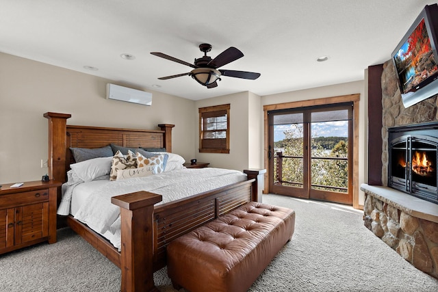 carpeted bedroom with ceiling fan, access to exterior, a wall mounted AC, and a stone fireplace