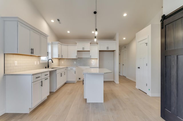 kitchen featuring pendant lighting, white cabinets, vaulted ceiling, a barn door, and a kitchen island