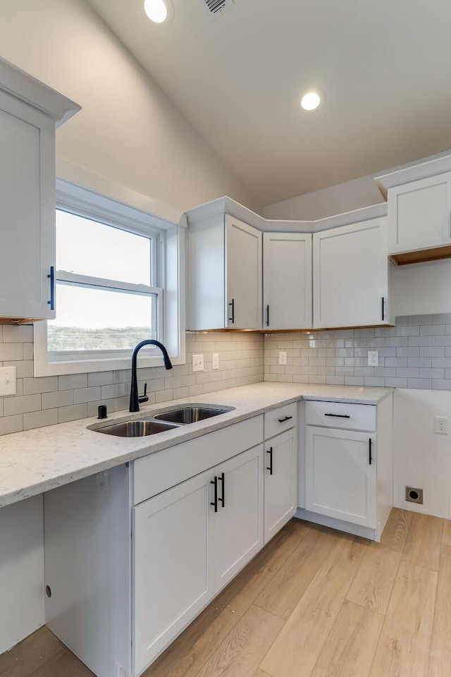 kitchen with lofted ceiling, backsplash, white cabinets, sink, and light hardwood / wood-style floors