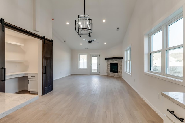 unfurnished living room featuring ceiling fan, a barn door, light wood-type flooring, and high vaulted ceiling