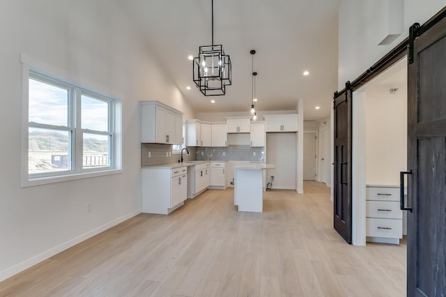 kitchen featuring light wood-type flooring, a barn door, high vaulted ceiling, a center island, and white cabinetry