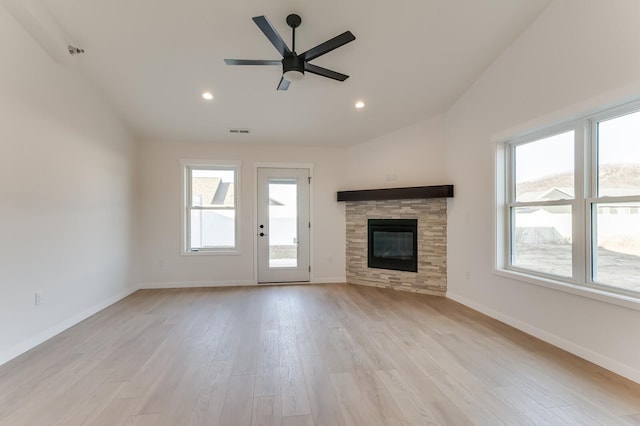 unfurnished living room with light hardwood / wood-style flooring, plenty of natural light, a stone fireplace, and ceiling fan