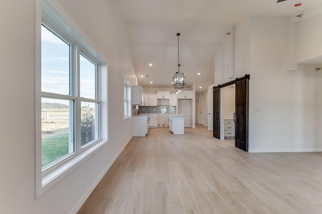 unfurnished living room featuring a barn door, light hardwood / wood-style floors, and an inviting chandelier