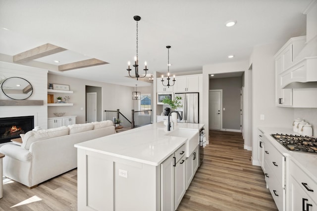 kitchen with a fireplace, a center island with sink, appliances with stainless steel finishes, a chandelier, and white cabinets