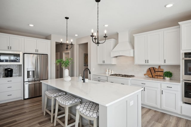 kitchen featuring white cabinets, appliances with stainless steel finishes, custom exhaust hood, and a notable chandelier