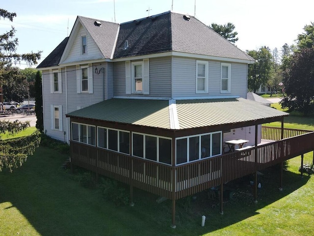 back of house featuring a deck, a lawn, and a sunroom