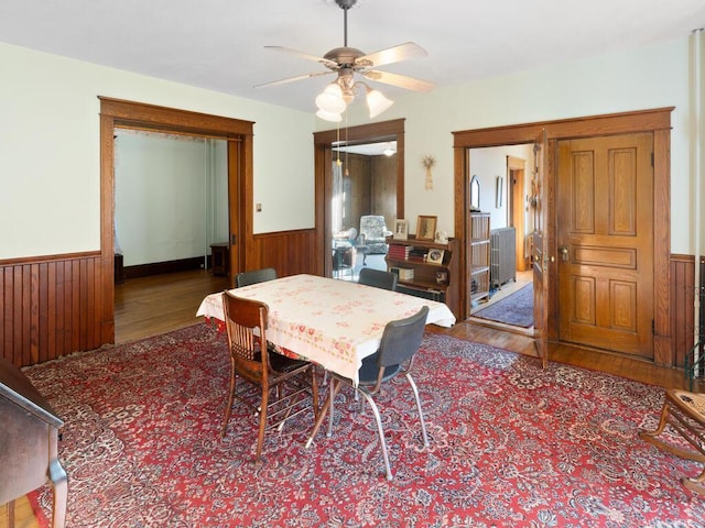 dining area with wood-type flooring, ceiling fan, and wood walls