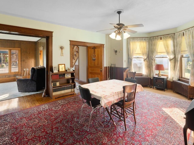 dining space with radiator, a wealth of natural light, wooden walls, and light hardwood / wood-style floors