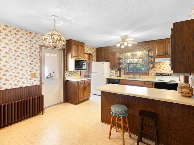 kitchen featuring radiator, range hood, a kitchen breakfast bar, black appliances, and a textured ceiling