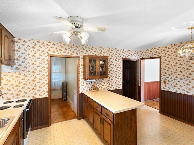 kitchen with hanging light fixtures, electric range oven, radiator heating unit, kitchen peninsula, and ceiling fan