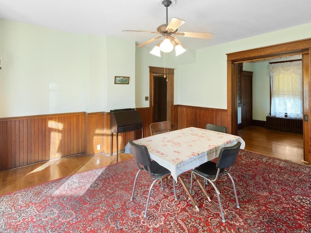 dining space with hardwood / wood-style flooring, ceiling fan, radiator, and wooden walls