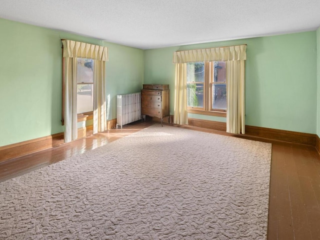 unfurnished room with radiator heating unit, hardwood / wood-style floors, and a textured ceiling