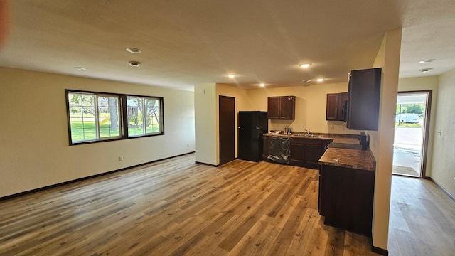 kitchen with sink, black fridge, light hardwood / wood-style flooring, dark stone counters, and dark brown cabinets