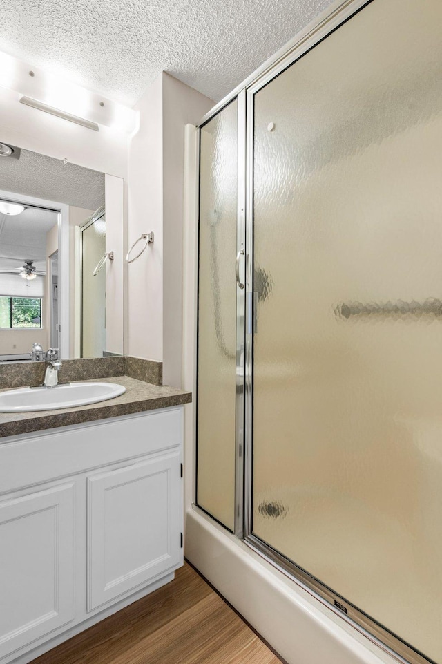 bathroom featuring hardwood / wood-style floors, walk in shower, vanity, a textured ceiling, and ceiling fan