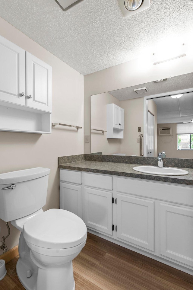 bathroom featuring toilet, a wall mounted AC, vanity, a textured ceiling, and wood-type flooring