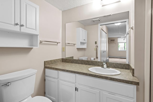 bathroom with a wall unit AC, a baseboard heating unit, toilet, vanity, and a textured ceiling