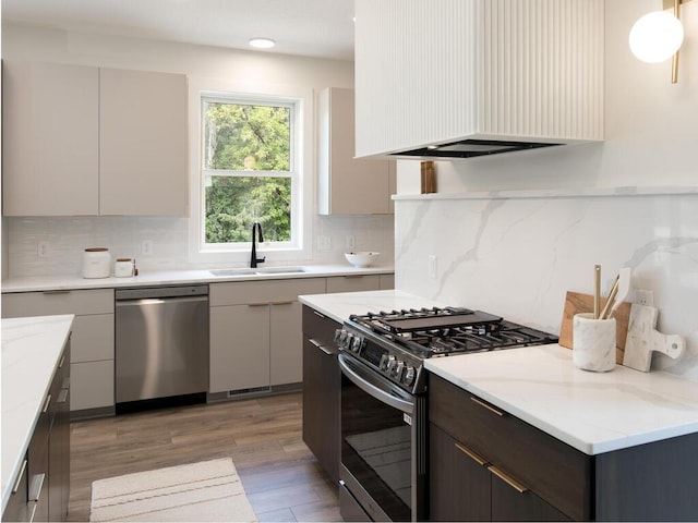 kitchen with light stone counters, dark brown cabinetry, wood-type flooring, white cabinetry, and appliances with stainless steel finishes