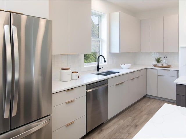 kitchen featuring appliances with stainless steel finishes, white cabinetry, backsplash, light wood-type flooring, and sink