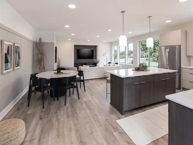 kitchen with light hardwood / wood-style flooring, dark brown cabinets, hanging light fixtures, and stainless steel fridge