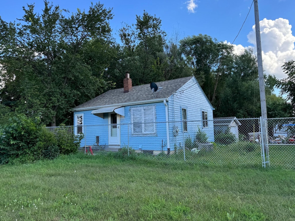 view of front of home with a shingled roof, a chimney, fence, and a front yard