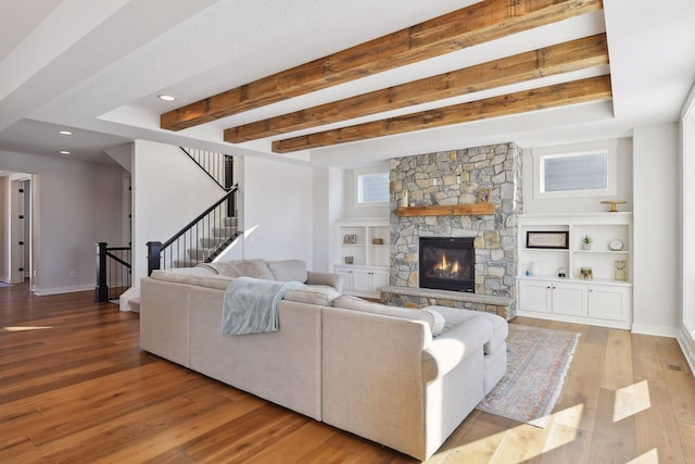 living room featuring beamed ceiling, light hardwood / wood-style floors, built in features, and a stone fireplace