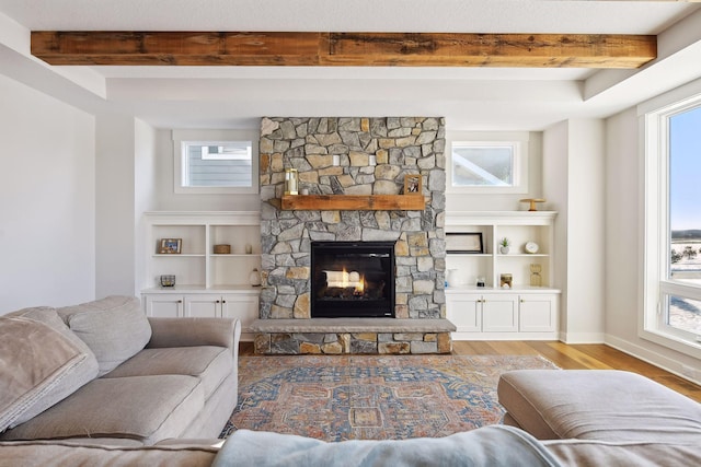 living room with light wood-type flooring, built in shelves, beam ceiling, and a stone fireplace