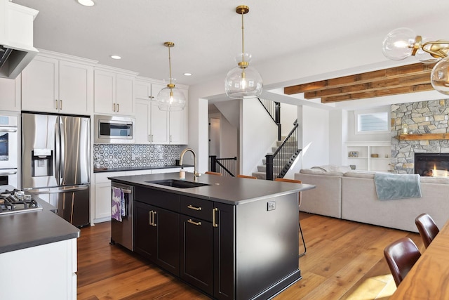 kitchen featuring appliances with stainless steel finishes, beamed ceiling, sink, a stone fireplace, and a center island with sink