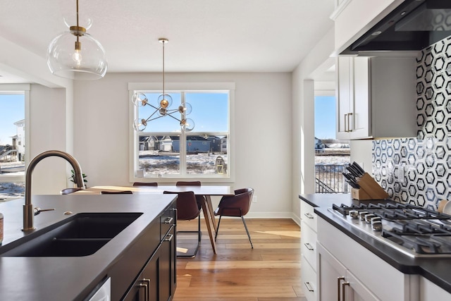 kitchen with white cabinets, hanging light fixtures, stainless steel gas stovetop, sink, and extractor fan