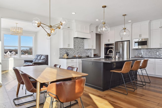 kitchen with a kitchen island with sink, appliances with stainless steel finishes, a chandelier, and light hardwood / wood-style floors