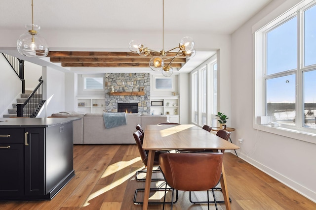 dining room with built in shelves, wood-type flooring, a fireplace, and a chandelier