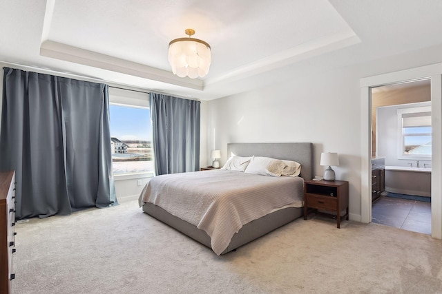 carpeted bedroom featuring ensuite bathroom and a tray ceiling