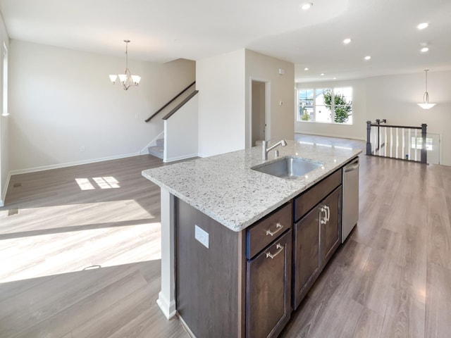 kitchen featuring pendant lighting, sink, stainless steel dishwasher, a kitchen island with sink, and light wood-type flooring