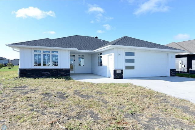 view of front of property with board and batten siding, a garage, concrete driveway, roof with shingles, and a front lawn