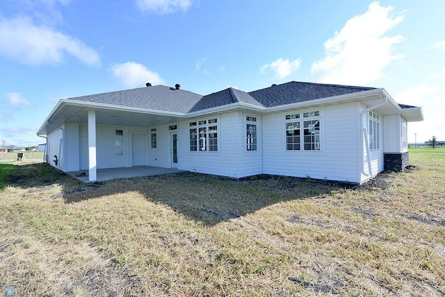 rear view of house with a patio area, roof with shingles, and a lawn