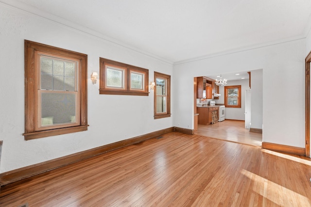 unfurnished living room featuring light wood-type flooring, crown molding, and an inviting chandelier