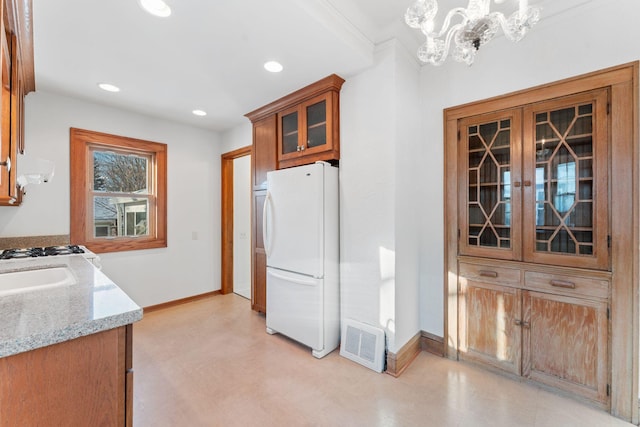 kitchen with white fridge, decorative light fixtures, light stone countertops, a chandelier, and sink