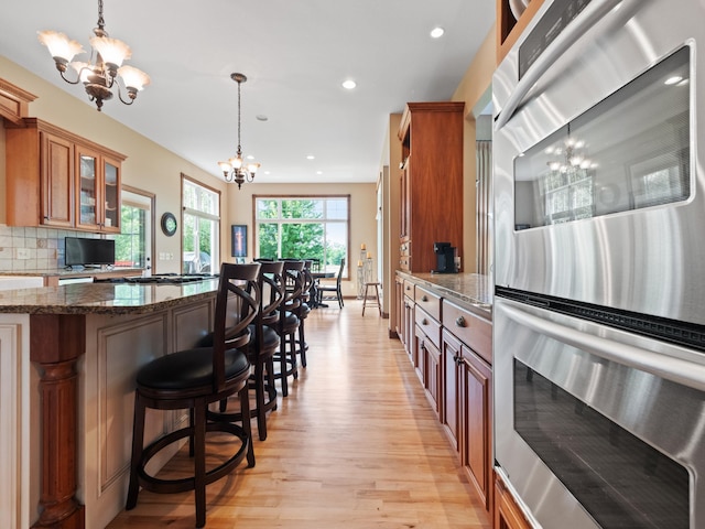 4424 Donway Dr NE, Alexandria, MN 56308 - kitchen with a chandelier, stainless steel double oven, brown cabinetry, light wood-style flooring, and a kitchen breakfast bar