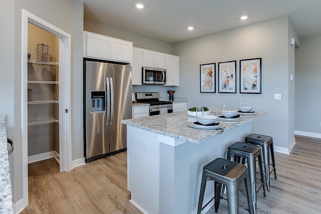 kitchen featuring white cabinetry, light hardwood / wood-style floors, stainless steel appliances, light stone counters, and a breakfast bar